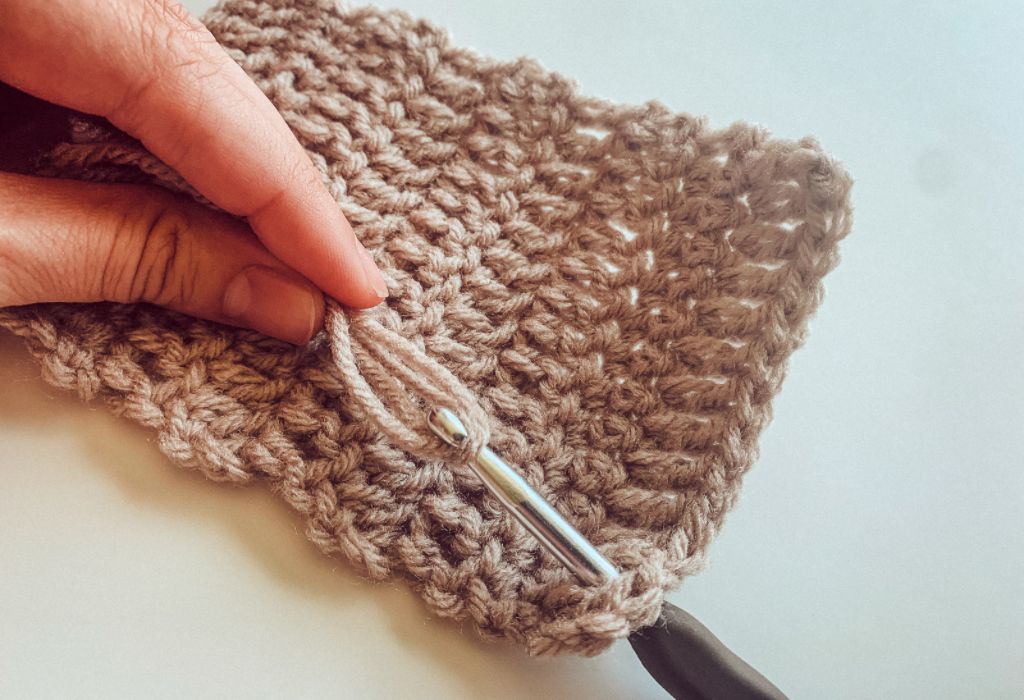 A crochet hook is pulling yarn through a crochet mug rug, a beginner crochet pattern, to make fringe