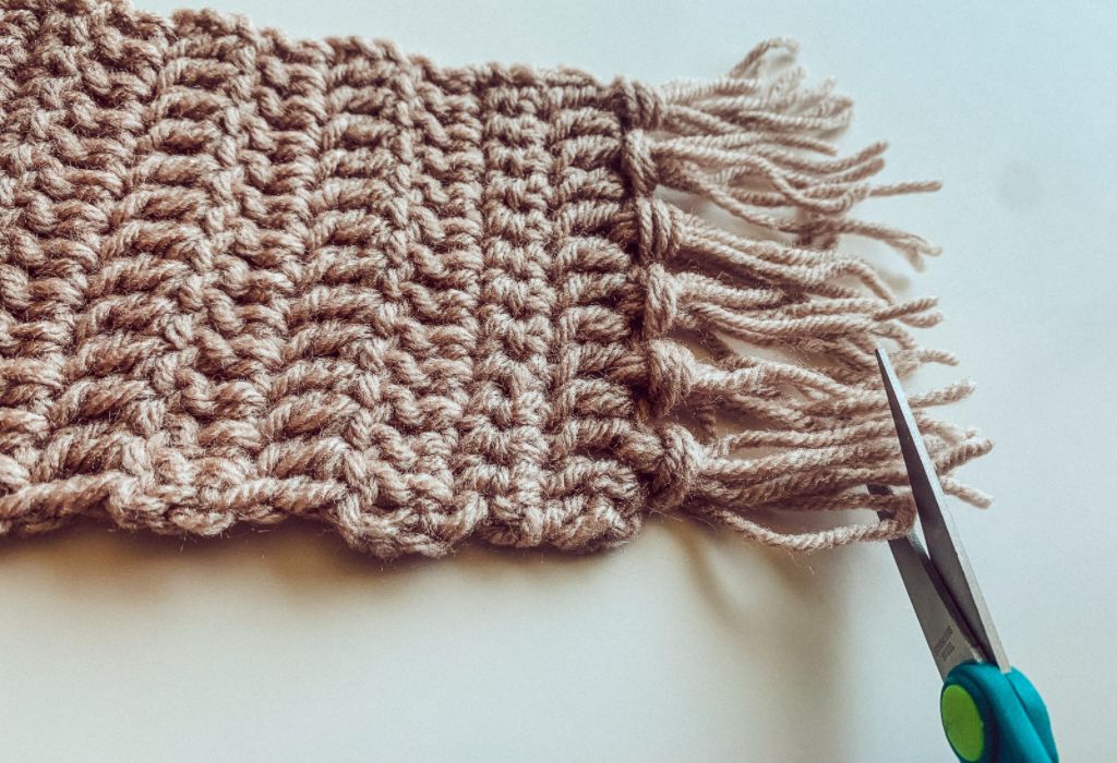 scissors are cutting the end of fringe on a crochet mug rug, a beginner crochet pattern