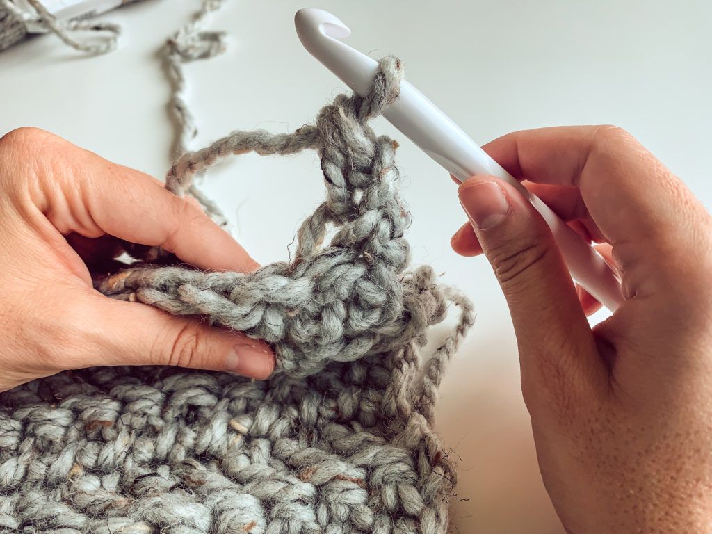 Two hands are shown crocheting a free modern crochet blanket pattern. The blanket is made with the herringbone double crochet stitch.