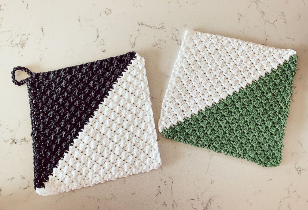 Two crochet pot holders made with the even moss stitch (one black and white, one green and white) are on a marble counter