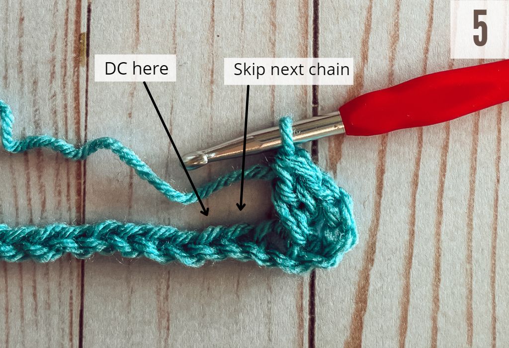 Image 5 of the crossed double crochet stitch tutorial. Yarn is blue and crochet hook is red. The background is whitewashed wood.