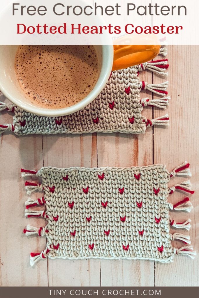 Two gray crocheted mug rugs with pink heart-shaped dots are on a wood background. They are made from a free crochet coaster crochet pattern. A mug filled with coffee is on the first mug rug/coaster. Text at the top says "free crochet pattern dotted hearts coaster" and text at the bottom reads "tinycouchcrochet.com"