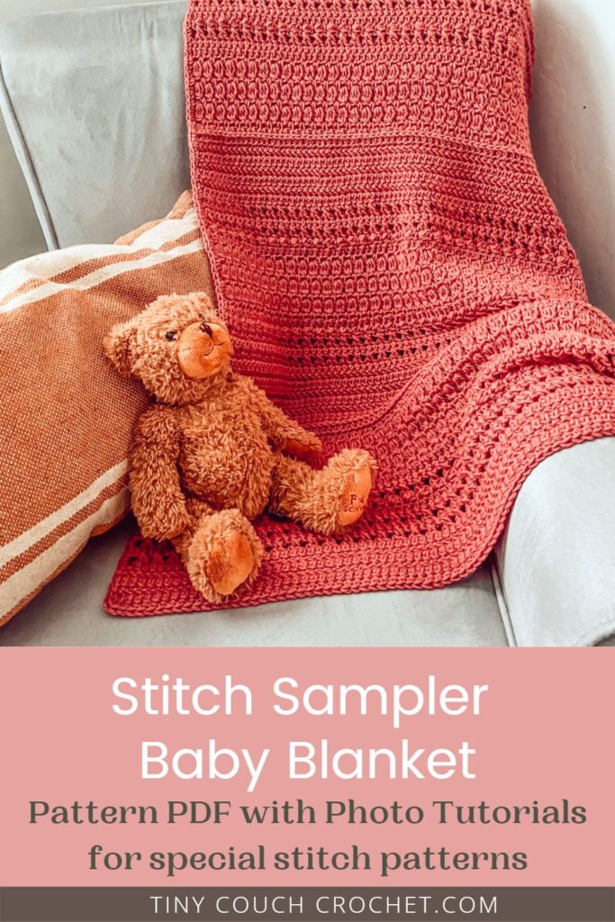A pink crochet baby blanket is draped over a gray chair. A pillow and teddy bear are also on the chair. Text reads "Stitch sampler baby blanket pattern PDF with photo tutorials for special stitch patterns tinycouchcrochet.com"